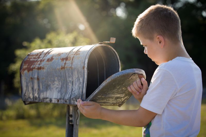 young boy checking his empty mailbox in the evening