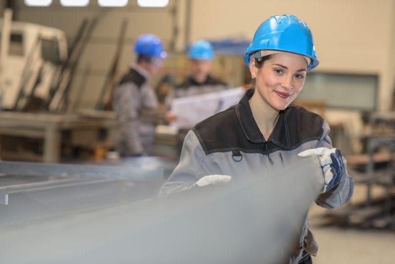 young woman working with large metal bars in a warehouse factory
