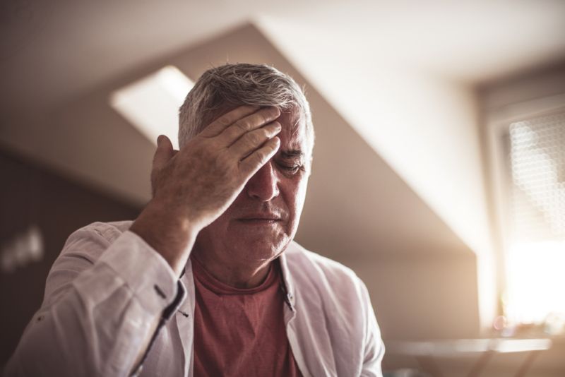 Old man experiencing a painful headache at home