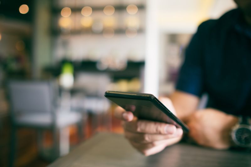 A man in a cafe scrolling on his cell phone