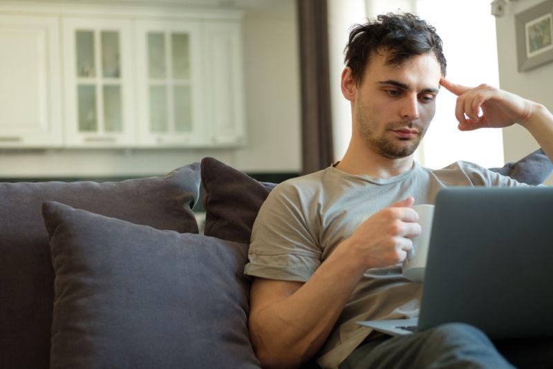 Tired man drinking coffee and using laptop